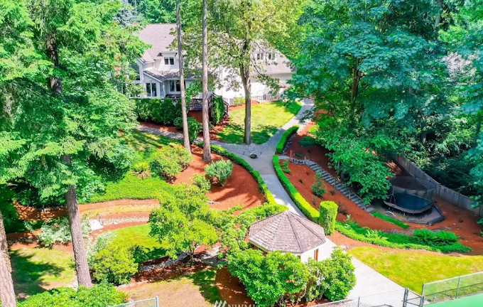 Aerial view of a large wooded residential property with freshly installed bark beds and winding paths